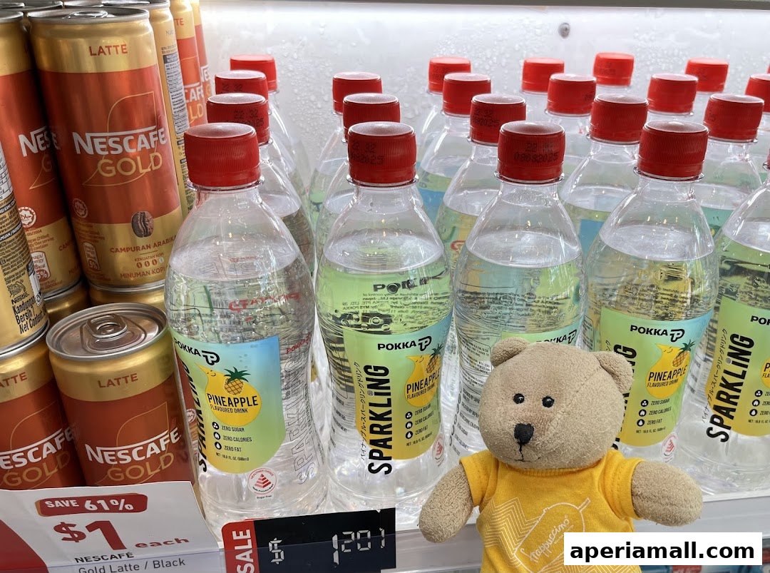 A display of Nescafe Gold Latte cans and Pokka Sparkling Pineapple drinks with a teddy bear.