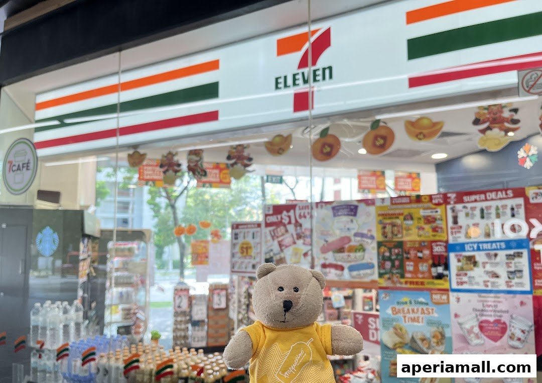 A teddy bear in a yellow shirt stands in front of a 7-Eleven store with various promotions displayed.