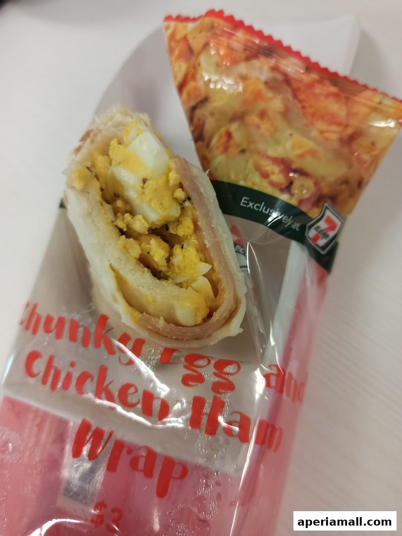 A close-up of a 7-Eleven Chunky Egg Chicken Ham Wrap with a side of potato chips.