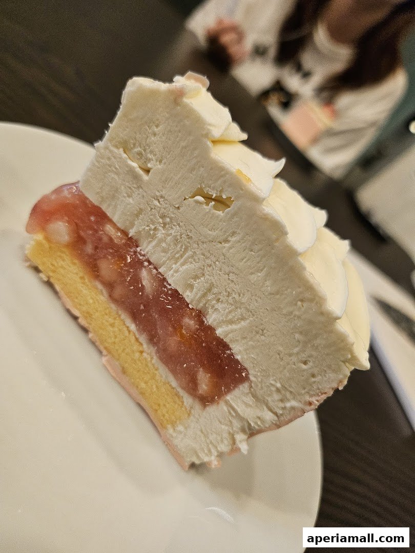 A slice of layered cake with white frosting and a pink fruit filling on a white plate.