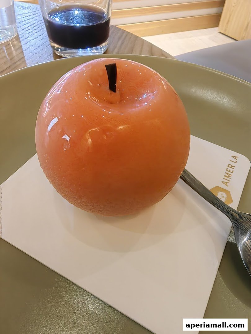 A close-up of a shiny, orange-glazed dessert shaped like an apple.