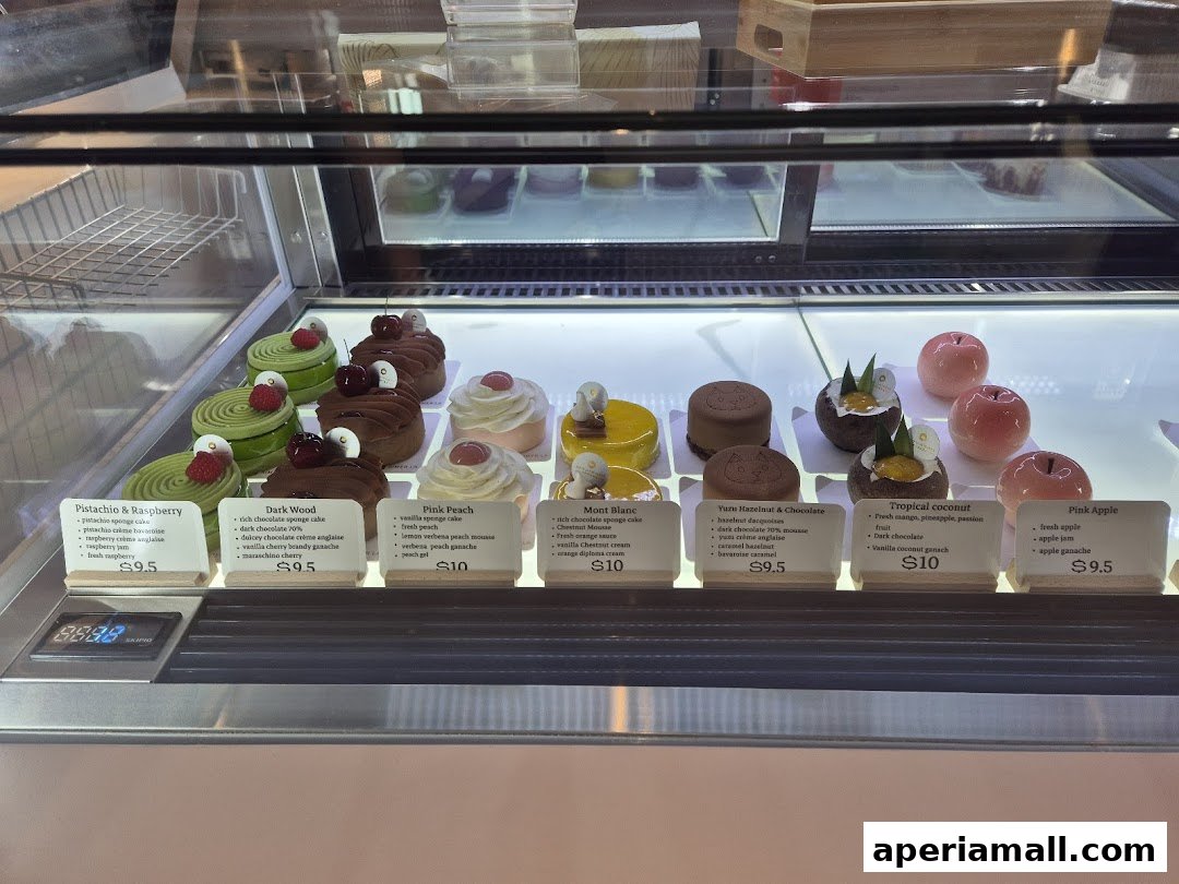A display case filled with beautifully crafted pastries and cakes, each with a descriptive label.