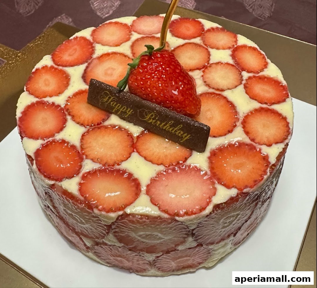 A beautifully decorated strawberry cake with a 'Happy Birthday' chocolate plaque and fresh strawberries.