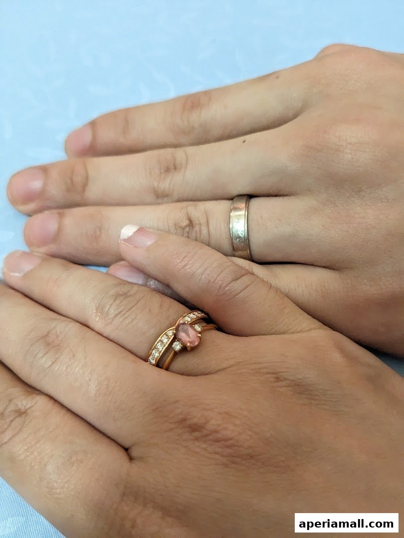 Close-up of two hands wearing wedding rings, one with a pink gemstone and diamonds.