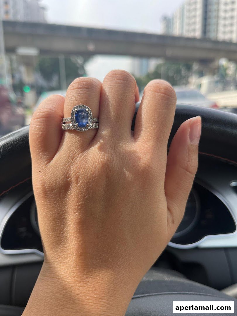 A hand wearing a sapphire and diamond ring, with a blurred city background.