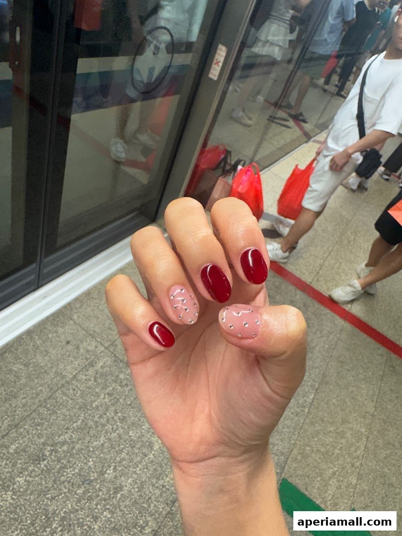 A hand with beautifully manicured nails, featuring a deep red polish and delicate crystal embellishments.