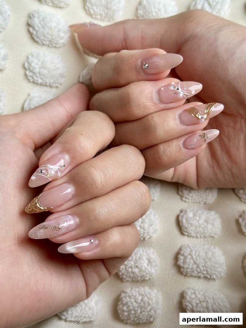 Close-up of hands with elegant, decorated fingernails featuring pearls, gold accents, and rhinestones.