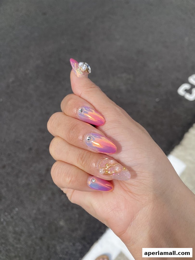 A hand with beautifully decorated nails featuring iridescent pink and purple polish and intricate embellishments.