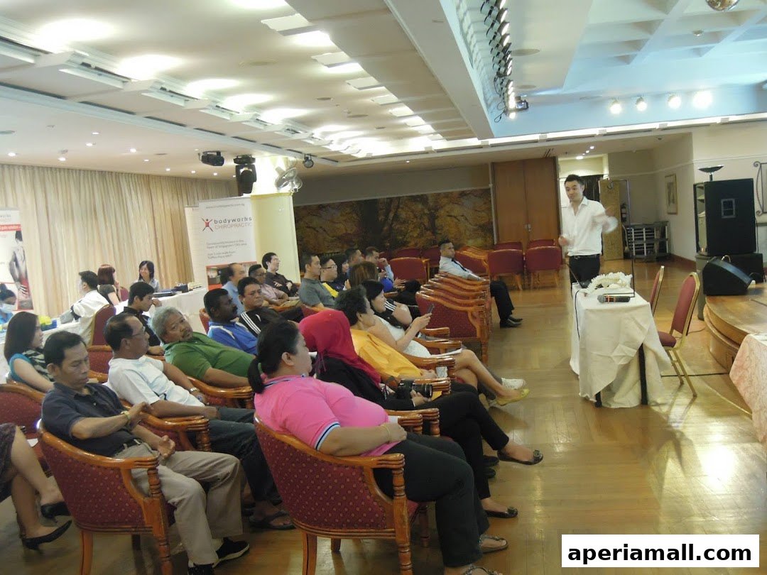 A speaker presents to an audience seated in chairs in a conference room.