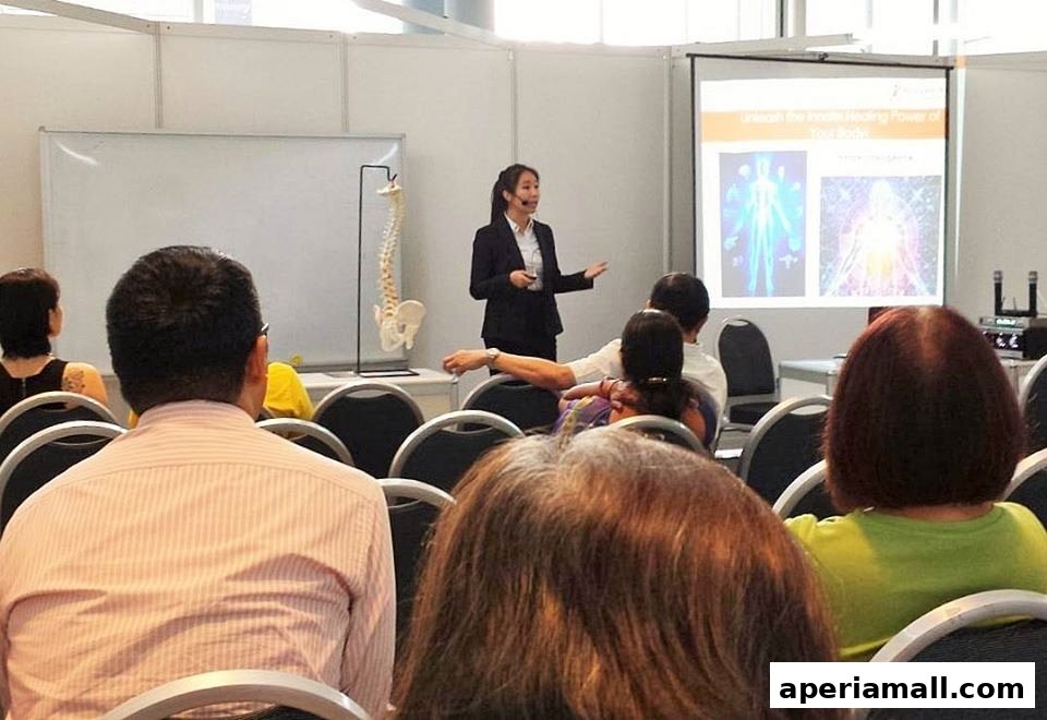 A presenter at Bodyworks Chiropractic Singapore is giving a talk with a spine model and presentation screen.