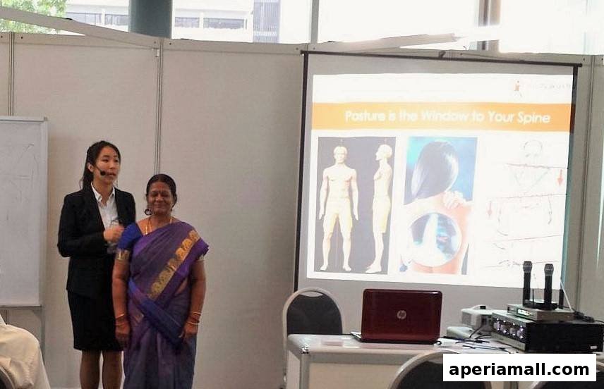 Two women stand near a projector screen displaying information about posture and the spine.