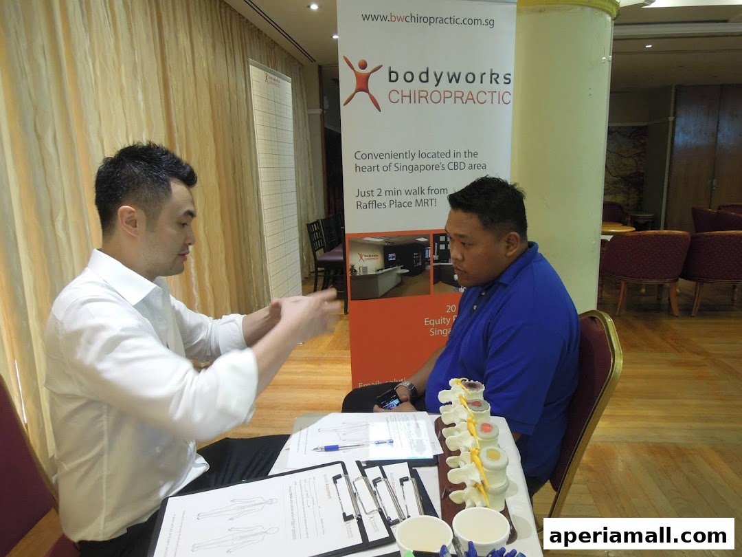 A chiropractor consults with a patient, with a spinal model and informational banner present.
