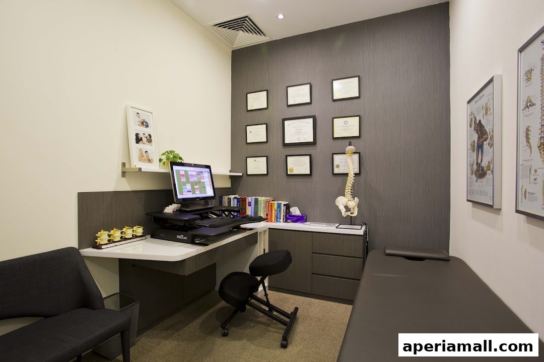 A chiropractic consultation room with a desk, computer, anatomical models, and a treatment table.