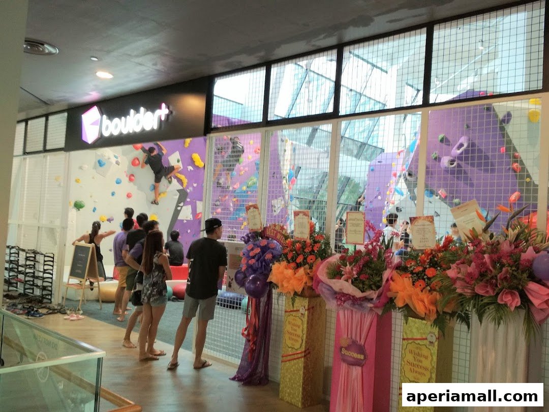 A bouldering gym with colorful climbing walls and people inside, with floral arrangements at the entrance.