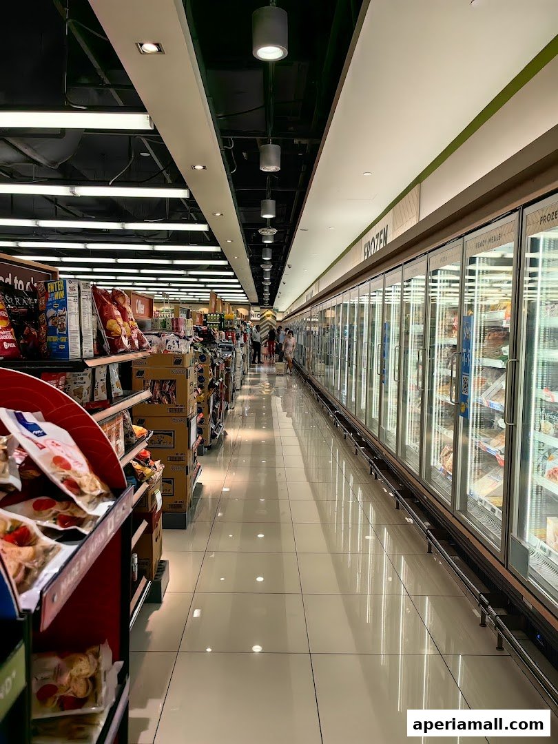 A long aisle in a supermarket with shelves of products and refrigerated display cases.