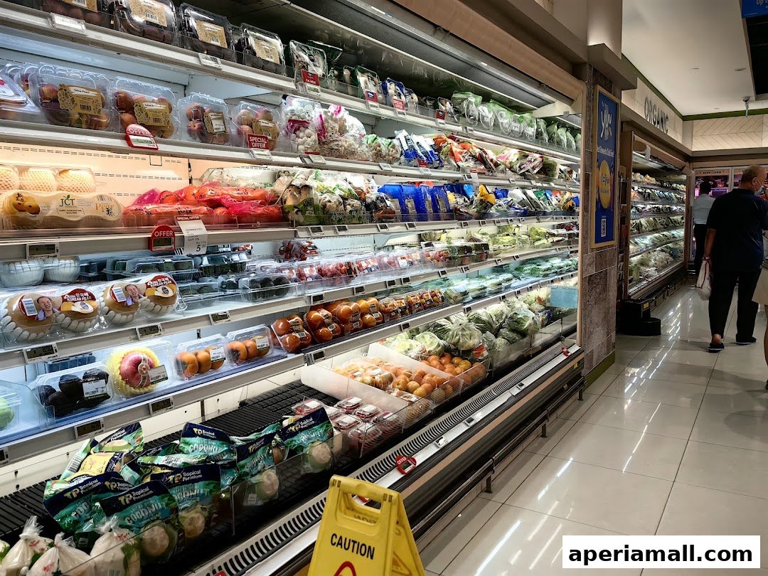 A wide aisle in a supermarket, showcasing fresh produce and packaged goods in refrigerated displays.