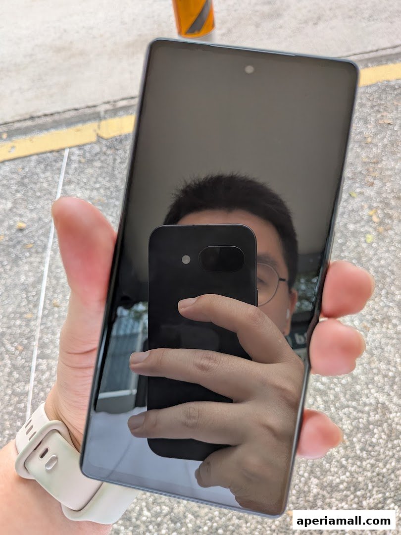 A person holds a smartphone, showing a reflection of their face and another phone.
