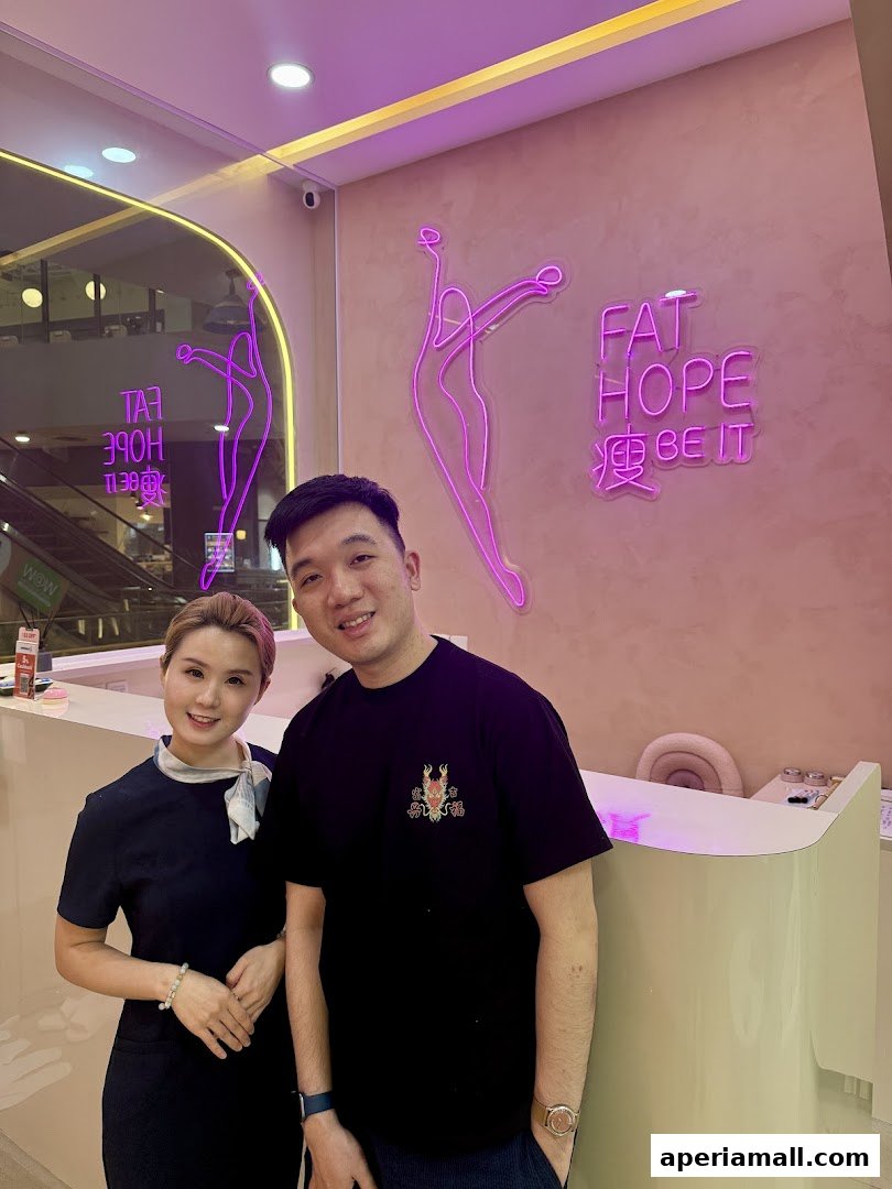 Two people smiling in front of a pink wall with neon signs and a reception desk.