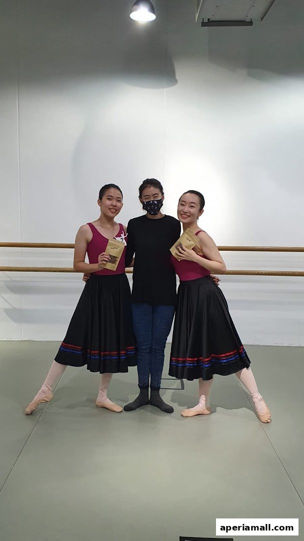 Two dancers and an instructor pose with small bags in a dance studio.