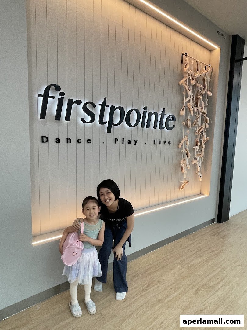 A woman and a young girl smile in front of the Firstpointe School of Dance sign.