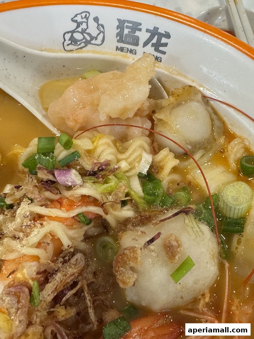 A close-up of a steaming bowl of seafood noodle soup with shrimp and scallops.