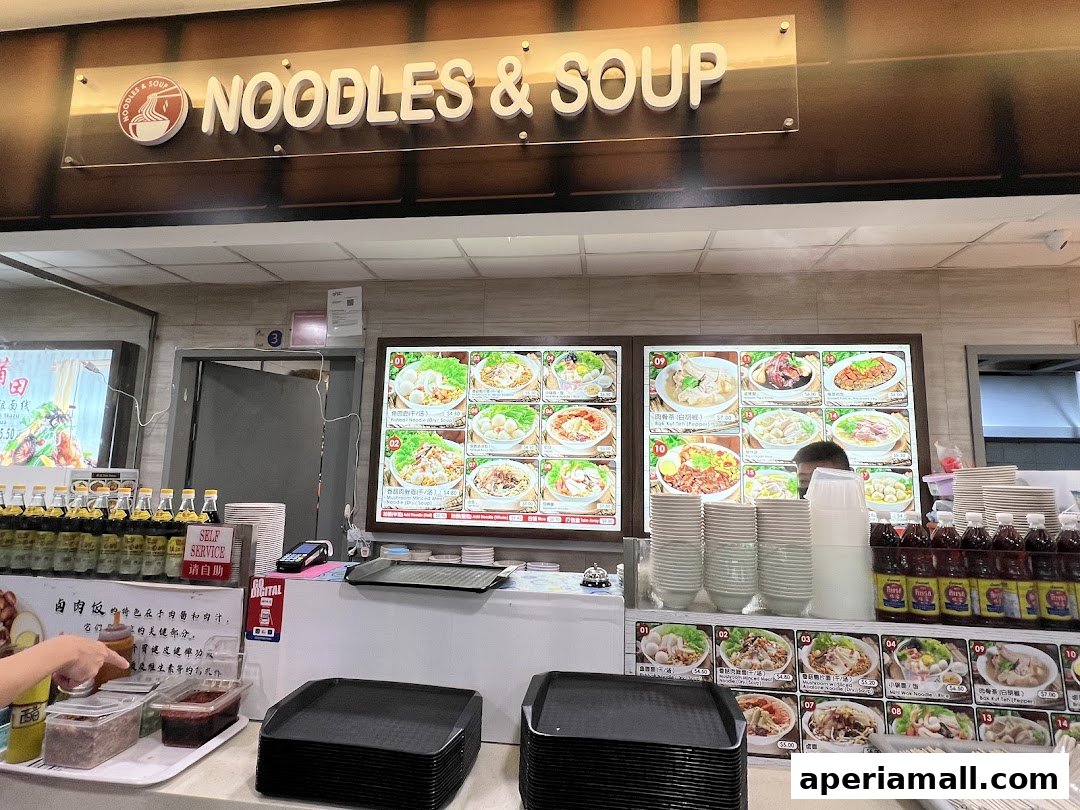 A food stall counter with digital menus displaying various noodle and soup dishes.