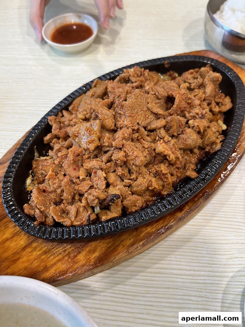 A sizzling plate of Korean bulgogi served with a side of dipping sauce and rice.