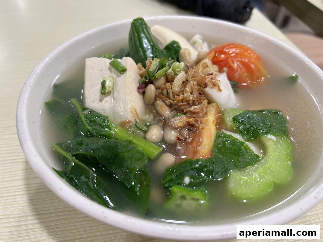 A close-up shot of a bowl of clear soup with tofu, vegetables, and beans.