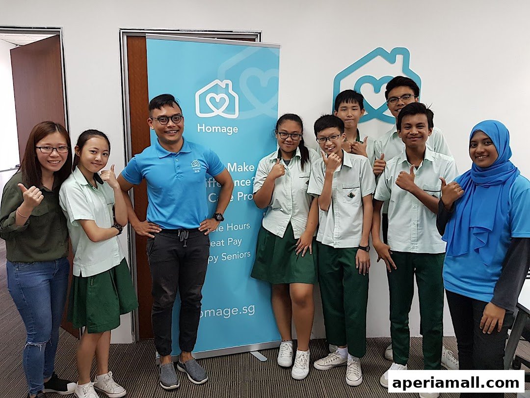 A group of young people and an adult pose for a photo in front of a Homage banner.