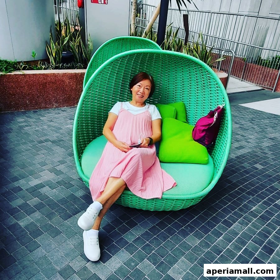 A woman in a pink dress relaxes in a green woven chair with bright green cushions.