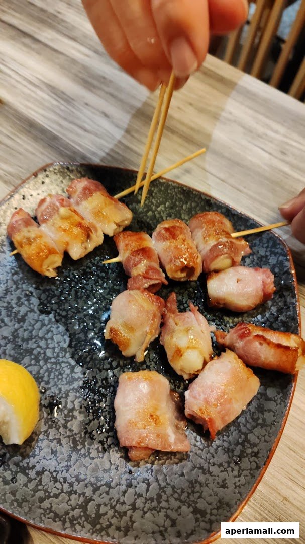 A plate of bacon-wrapped skewers with a lemon wedge.