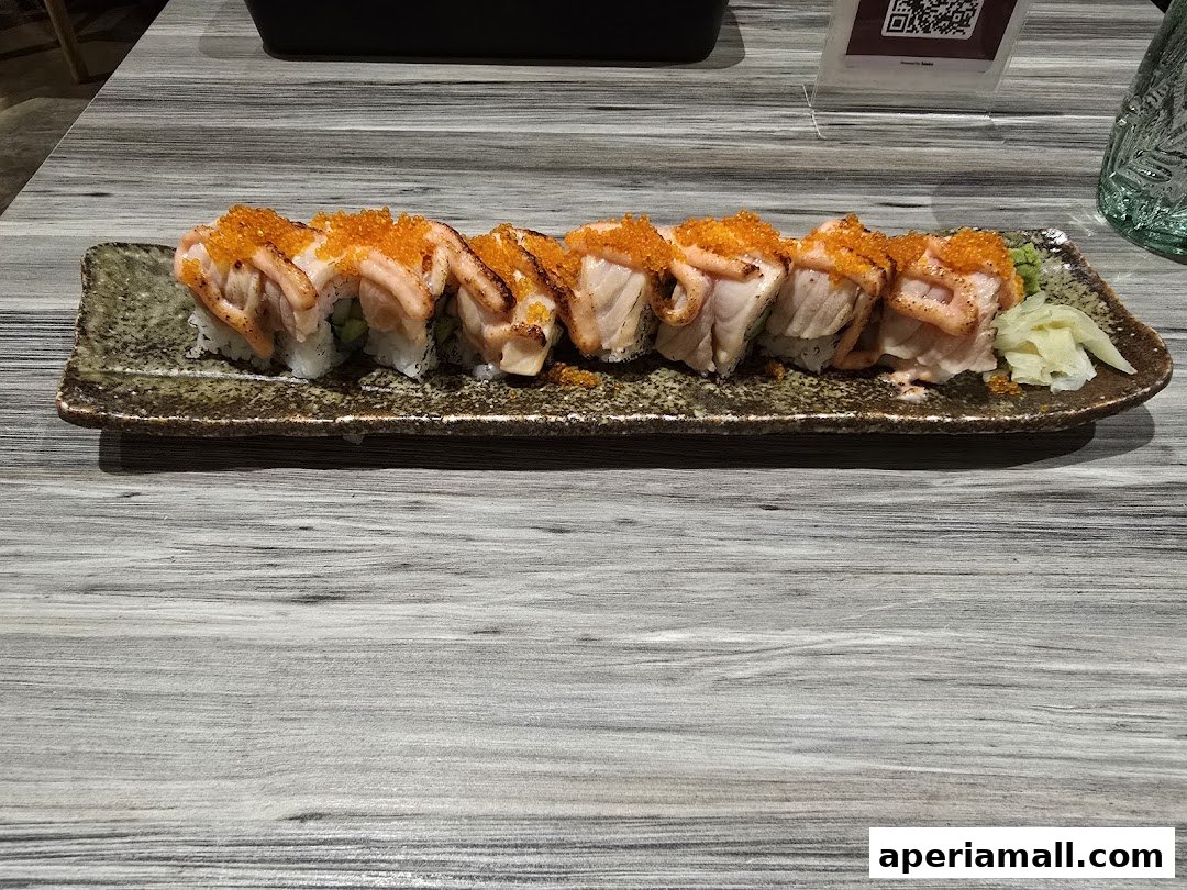 A plate of sushi rolls topped with torched salmon and orange roe, served with pickled ginger.