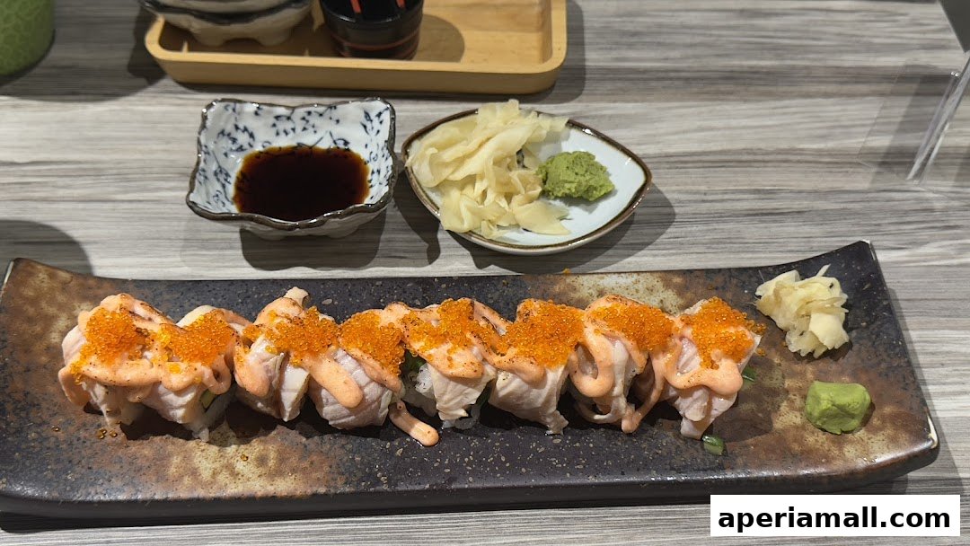 A plate of sushi rolls topped with torched salmon and tobiko, served with soy sauce, wasabi, and ginger.