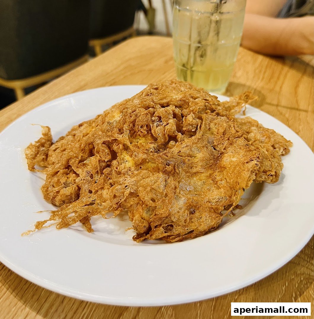 A close-up of a crispy, golden-brown omelet served on a white plate with a drink in the background.