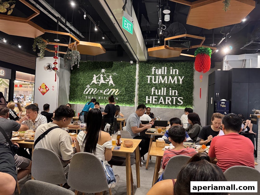 A busy Thai restaurant interior with diners enjoying their meals and a green wall with the restaurant's logo.