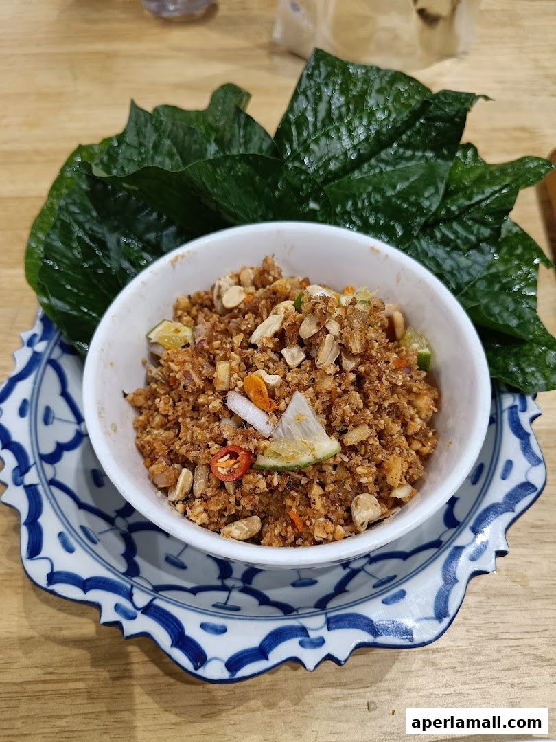 A close-up of a Thai dish served in a white bowl on a decorative blue and white plate, garnished with peanuts and chili.