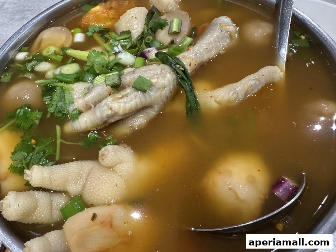 A close-up of a steaming bowl of Thai chicken feet soup with herbs and meatballs.