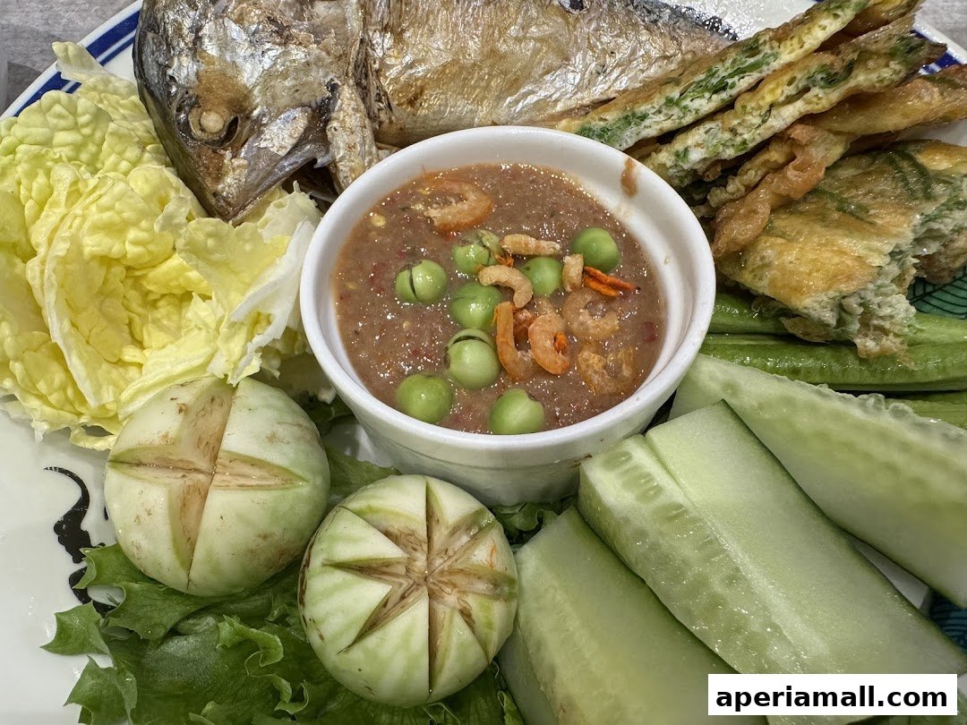 A plate of Thai food featuring fried fish, dipping sauce, vegetables, and omelet.