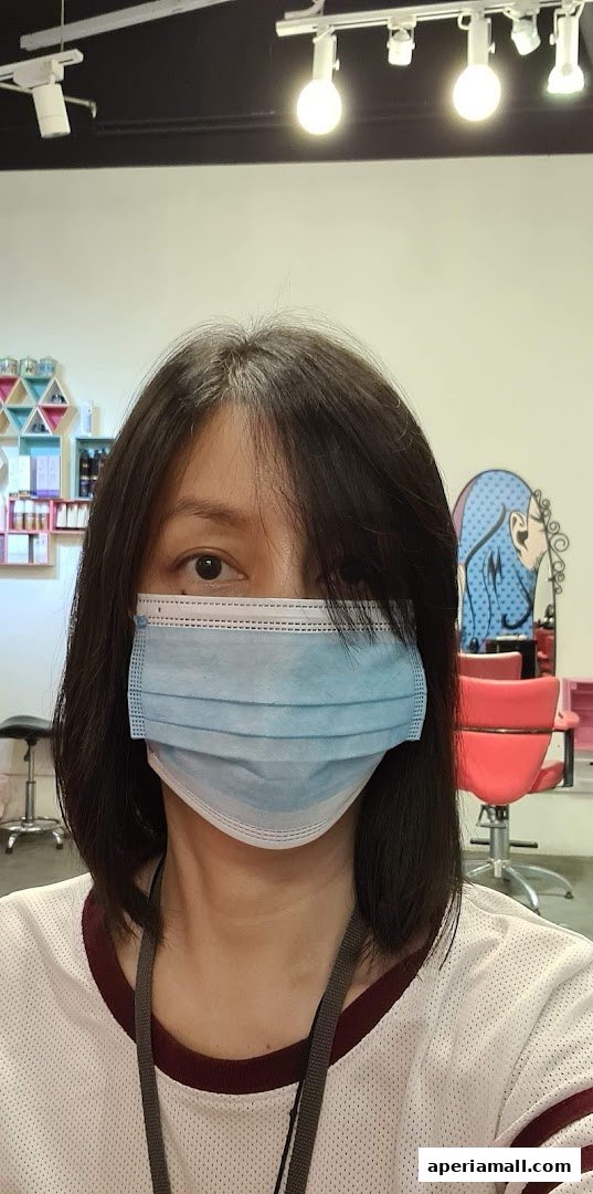 A person wearing a face mask in a hair salon with styling chairs and products visible.