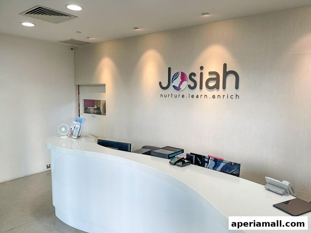 The reception area of Josiah Montessori Aperia features a modern white counter with the company logo on the wall.