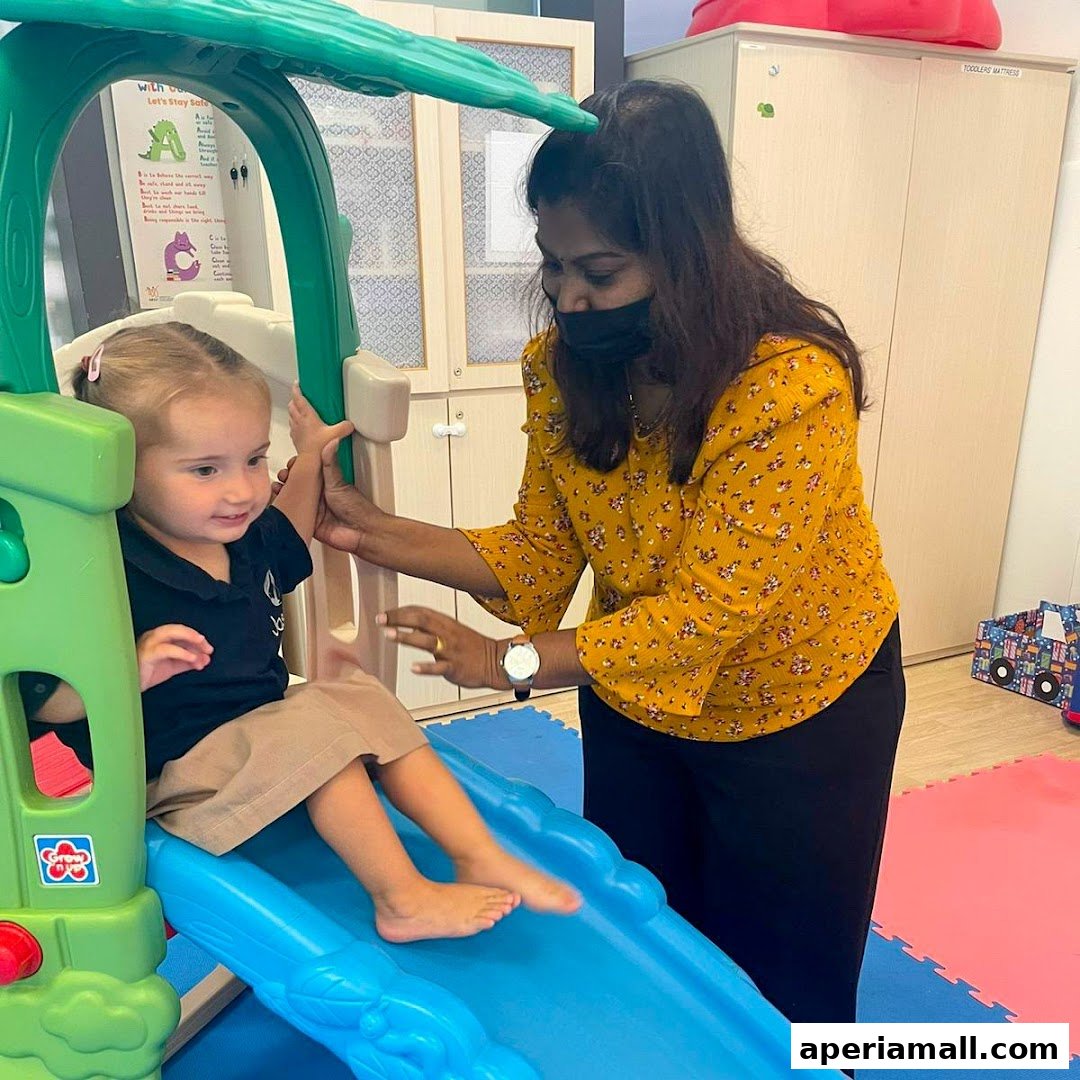 A teacher assists a young child on a slide in a bright, child-friendly learning environment.