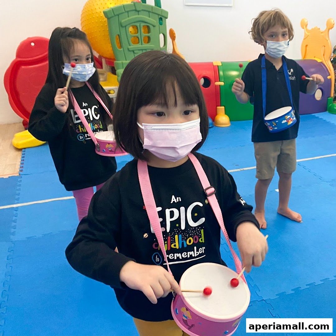 Children wearing masks play drums in a brightly lit room with colorful play equipment.