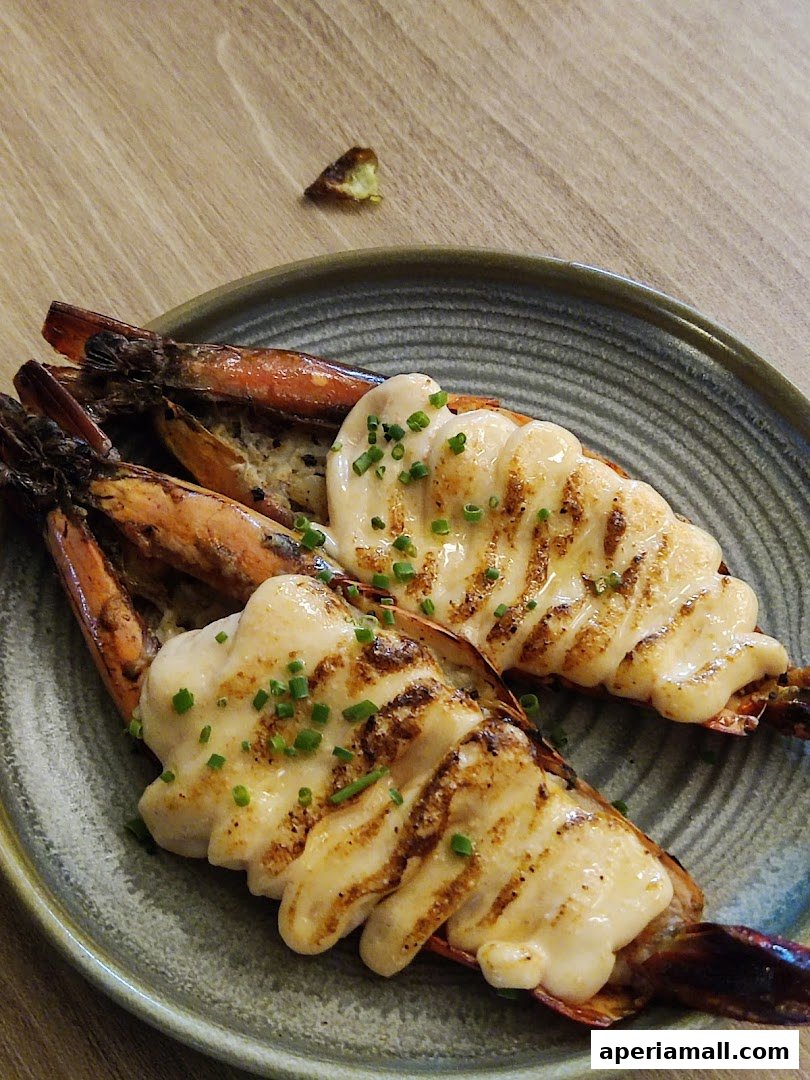 Two grilled prawns topped with creamy sauce and chives on a plate.