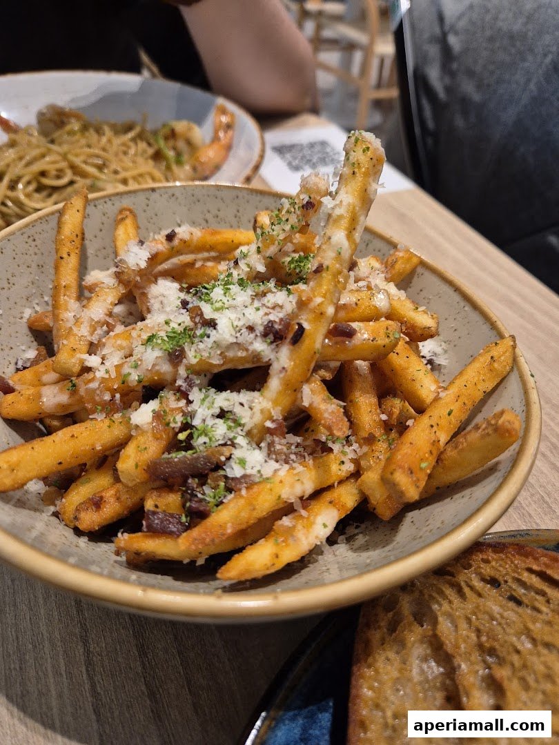 A close-up of a bowl of loaded fries topped with cheese and herbs, with other dishes blurred in the background.