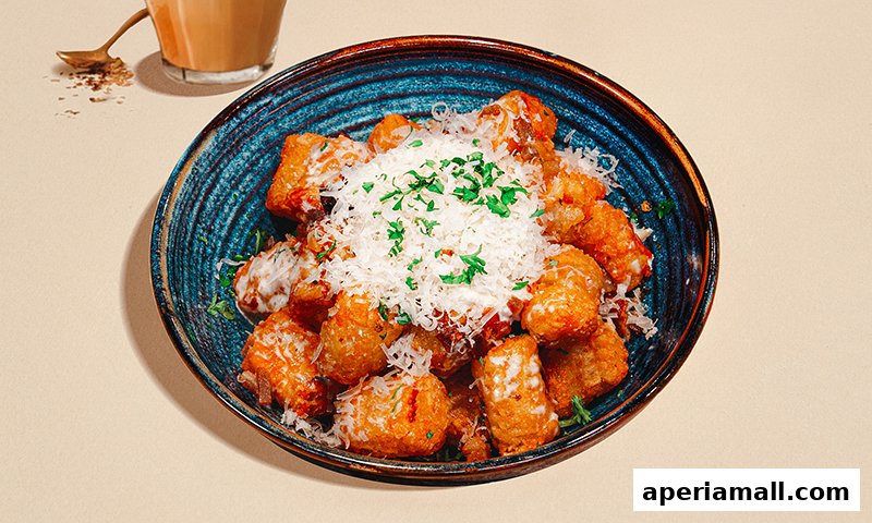 A close-up of a bowl of crispy tater tots topped with shredded cheese and parsley.