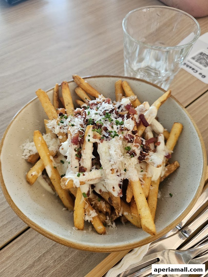 A bowl of loaded fries topped with cheese, bacon, and chives, served with a glass of water.