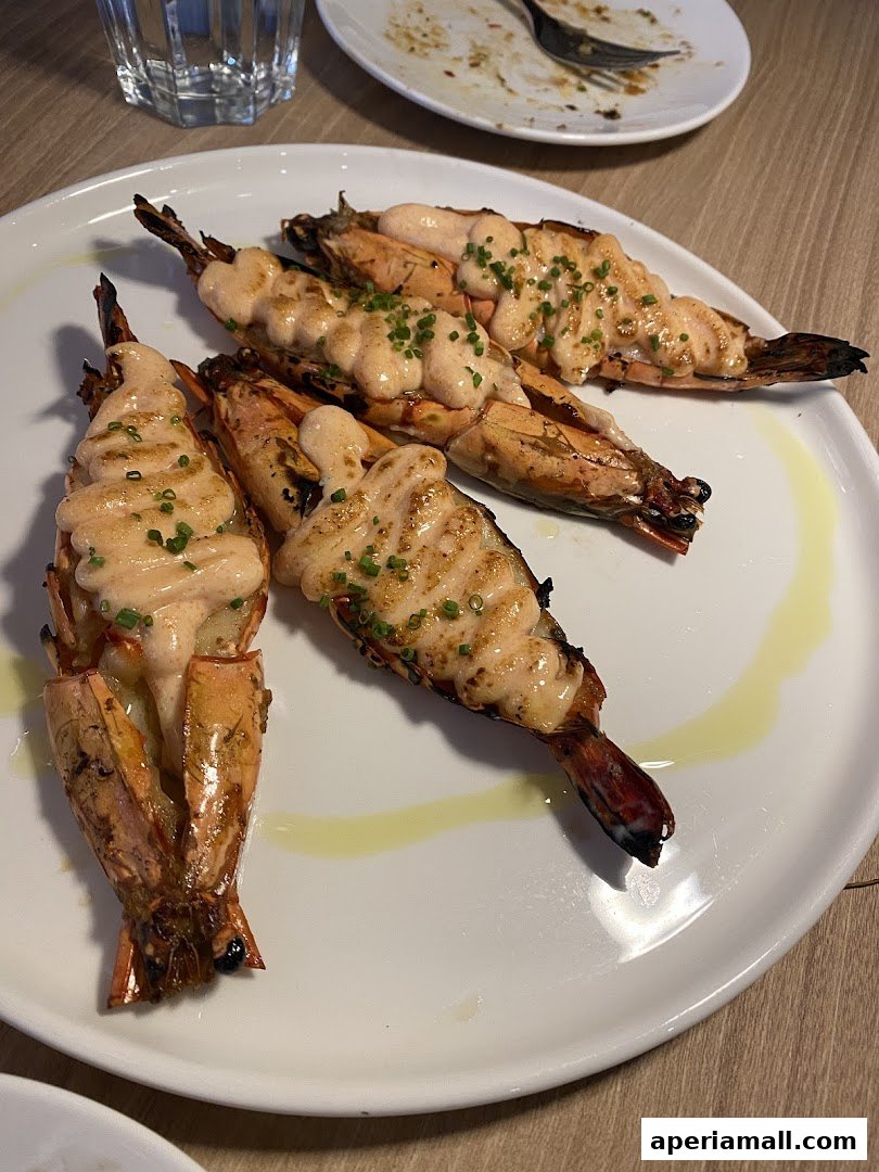 A plate of grilled prawns topped with a creamy sauce and chives, served with a glass of water.