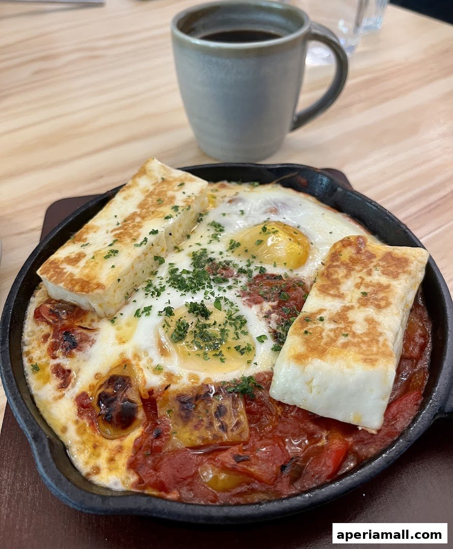 A hearty breakfast dish with eggs, cheese, and tomatoes served in a cast-iron skillet with a cup of coffee.