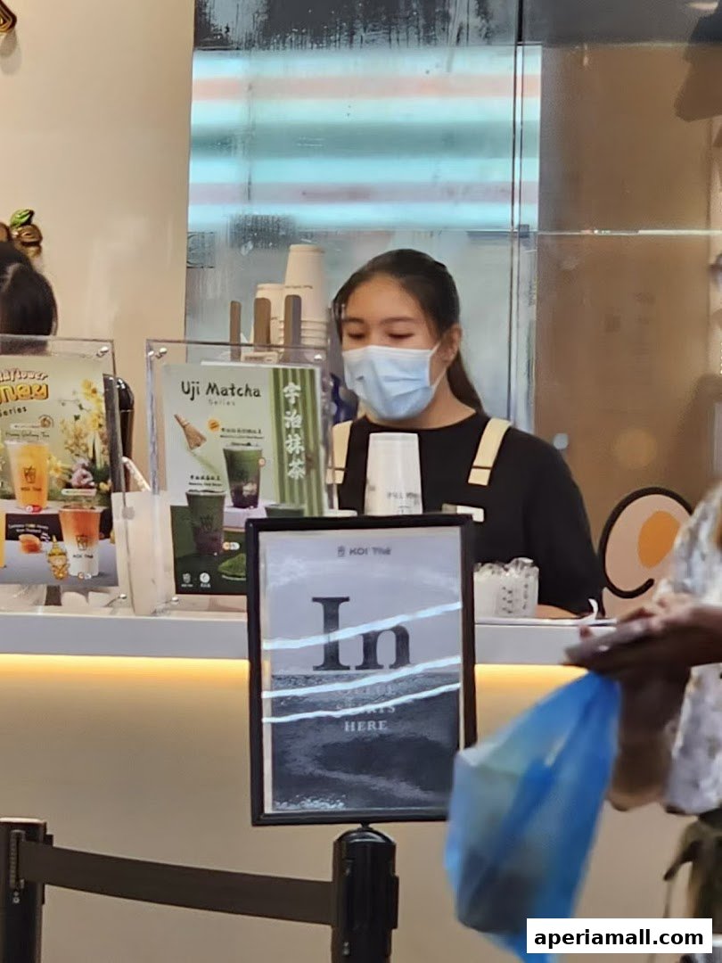 A young woman wearing a mask serves drinks at a KOI Thé counter.