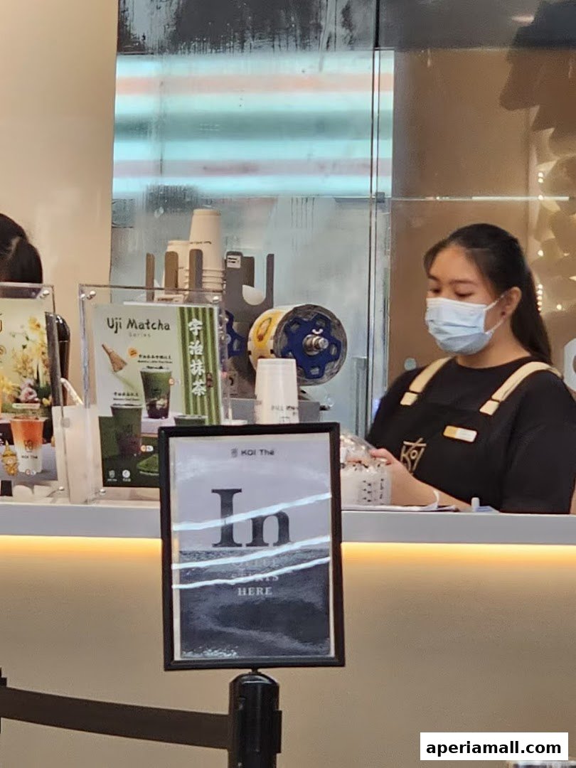 A staff member at KOI Thé prepares drinks behind a counter with promotional materials.